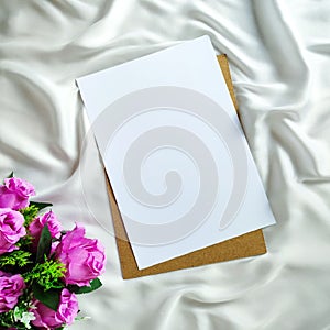 Top view of blank piece of paper and artificial flowers on the white piece of cloth