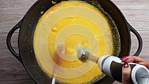 Top view of the blender mixing a pumpkin soup puree in the pan