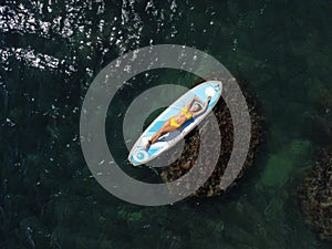 Top view on blonde woman in yellow bikini relaxing on the sup board. Young attractive woman in the sea on the Stand Up