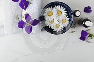 Top view of blue bowl and flowers in it, white towels, purple flowers, bottles on the marble surface.Empty space