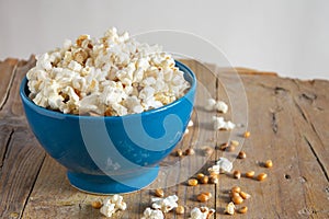 Top view of blue bowl with fresh popcorn on rustic wooden table, white background, horizontal