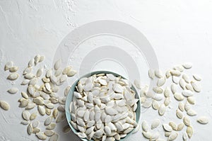 Top view of blue bowl full of pumpkin seeds on the white table.Empty space for text