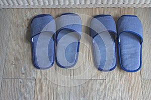 Top view blue comfortable slippers two pairs on wooden floor in the bedroom.