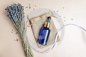 top view of blue glass dropper bottle vith lavender aromatic essential oil or extract on beige background. Bunch of scented dry