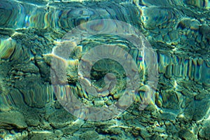 Top view of blue, green and turquoise colors of water, surface of sea on rocks and bottom. Reflection of sun beams in water.