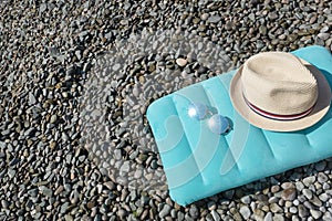Top view of blue inflatable swimming pillow, sunglasses and sun hat lie on stone seaside near sea.