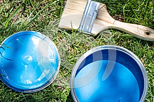 Top view of blue paint can, can lid, new brush on green grass