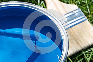 Top view of blue paint can, can lid, new brush on green grass