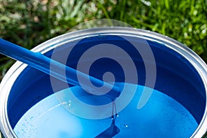 Top view of blue paint can, can lid, new brush on green grass