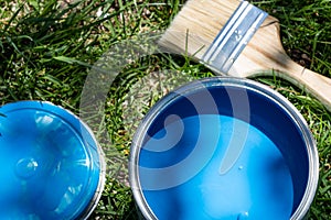 Top view of blue paint can, can lid, new brush on green grass