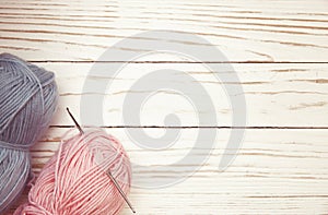 Top view of blue and pink wool balls of thread and crochet hook on white wooden knitting background