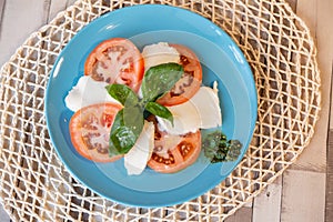 Top view of a blue plate with fresh tomato, basil leaves, and cheese