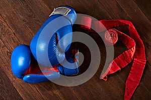 Top view of blue and red boxing gloves and bandage on wooden plank background.