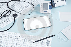 Top view of blue table with blank cellphone, stethoscope, cardiogram, pen, other items and mock up place. Doctor`s office,