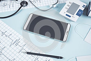 Top view of blue table with blank phone, stethoscope, cardiogram, pen, other items and mock up place. Doctor`s office, workplace