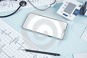 Top view of blue table with blank smart phone, stethoscope, cardiogram, pen, other items and mock up place. Doctor`s office,