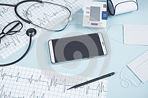 Top view of blue table with blank smartphone, stethoscope, cardiogram, pen, other items and mock up place. Doctor`s office,