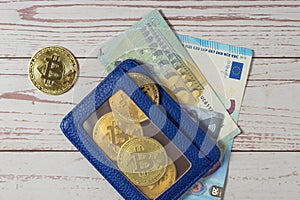 Top view of a blue wallet with Bitcoin coins, Euro bills and a bank card on a wooden background. Close-up