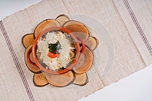 Top view of boiled rice with greens and tomato in a bowl on round woodcuts on a tablecloth