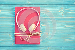 Book and new modern pink music headphone on blue wooden plank ba
