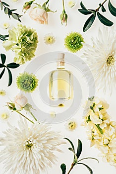 top view of bottle of aromatic perfume surrounded with flowers and green branches