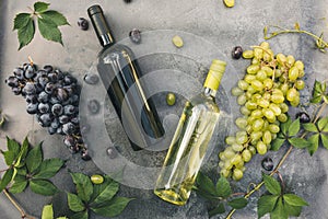 Top view of bottle red and white wine, green vine, wineglass and ripe grape on vintage dark stone table background. Wine