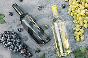 Top view of bottle red and white wine, green vine, wineglass and ripe grape on vintage dark stone table background. Wine