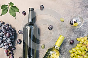 Top view of bottle red and white wine, green vine, wineglass and ripe grape on vintage dark stone table background. Wine