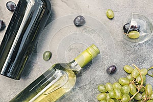 Top view of bottle red and white wine, green vine, wineglass and ripe grape on vintage dark stone table background. Wine