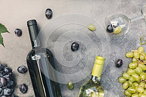 Top view of bottle red and white wine, green vine, wineglass and ripe grape on vintage dark stone table background. Wine