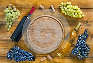 Top view of  bottle of wine,  bunch of grapes and  round cutting board