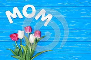 top view of bouquet of pink and white tulips and word mom on blue table, mothers day concept