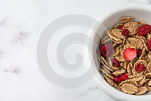 Top view of bowl with cereals and red berries on white marble table, horizontal