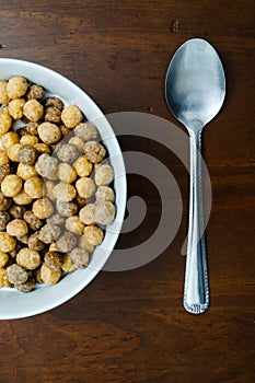 Top view of a bowl of cereals and a silver spoon on a wooden table