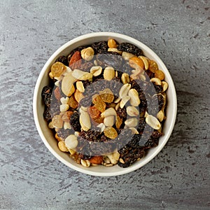 Top view of a bowl filled with high energy trail mix on a gray mottled background in natural light