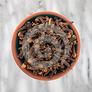 Top view of a bowl filled with whole cloves on a marble countertop