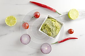 Top view of bowl with fresh made quacamole and different ingredients on marble table in the kithen