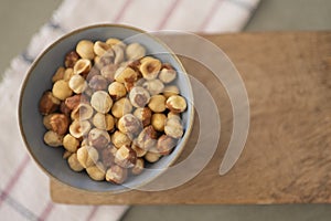 Top view of bowl of hazelnuts on wood board with a napkin in the background