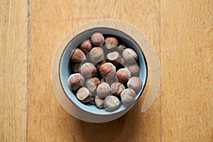 Top view of a bowl of hazelnuts on a wooden table in a blurred background