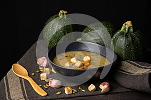 Top view of a bowl of homemade zucchini cream with pumpkin seeds, bread and paprika, on a table with dark cloth, garlic