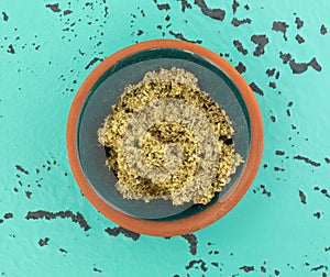 Top view of a bowl with a small portion of crushed sage leaf atop a green and black tabletop