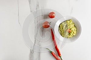 Top view of bowl with tasty guacamole with chilli pepper and tomatoes served on white table in the kitchen,empty space