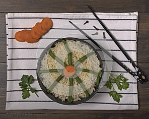 Top view of a bowl of white rice with green beans, carrots, cloves and parsley