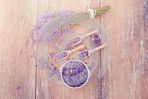 Top view of a bowl and wooden spoons with fresh lavender flowers and a bouquet of lavender on a brown wooden background