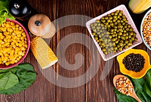 top view of bowls of green peas corn seeds and black pepper with spinach on wooden background