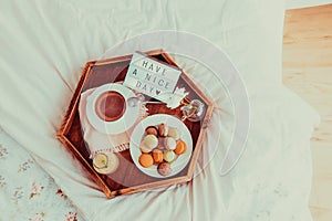 Top view Breakfast in bed with Have a nice day text on lighted box. Coffee, juice, macaroons, flower in vase on wooden tray. Good