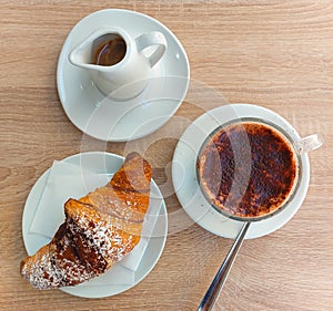 Top view of a breakfast with chocolate croissant, milk with cocoa powder and coffee