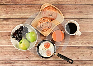 Top view of breakfast set , black coffee , orange juice, fried eggs,danish pastry and croissant, two apples and grape on wooden