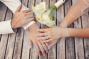 Top view of bride and groom hands with the engagement rings, and bouquet of white callas on rustic wooden table background