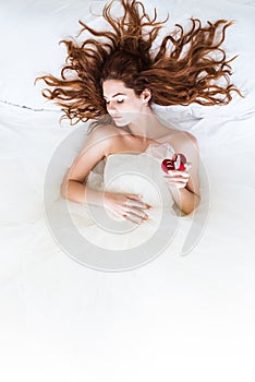 Top view of bride wearing white dress sleeping in bed and holding